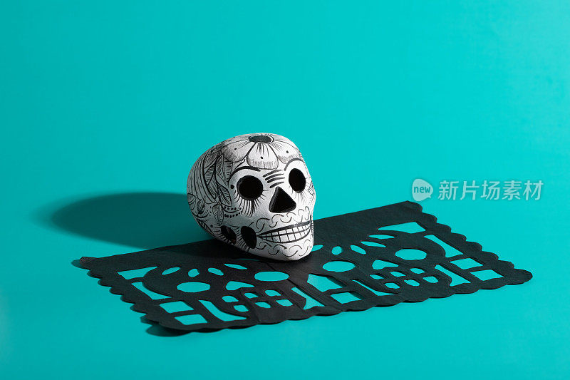 死亡的陶器头骨(calavera)在黑色papel picado在蓝绿色背景，Dia de Muertos背景